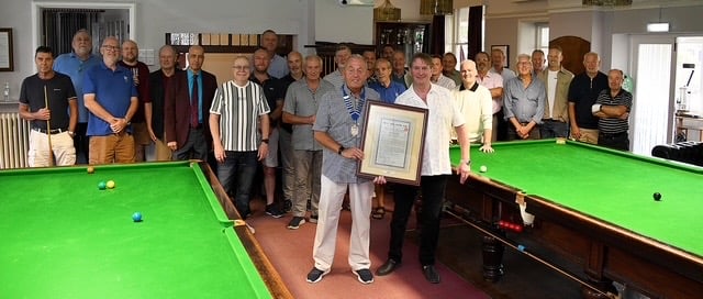 A group of members in the club's snooker room, two of them at the centre holding a framed debenture certificate above the table.