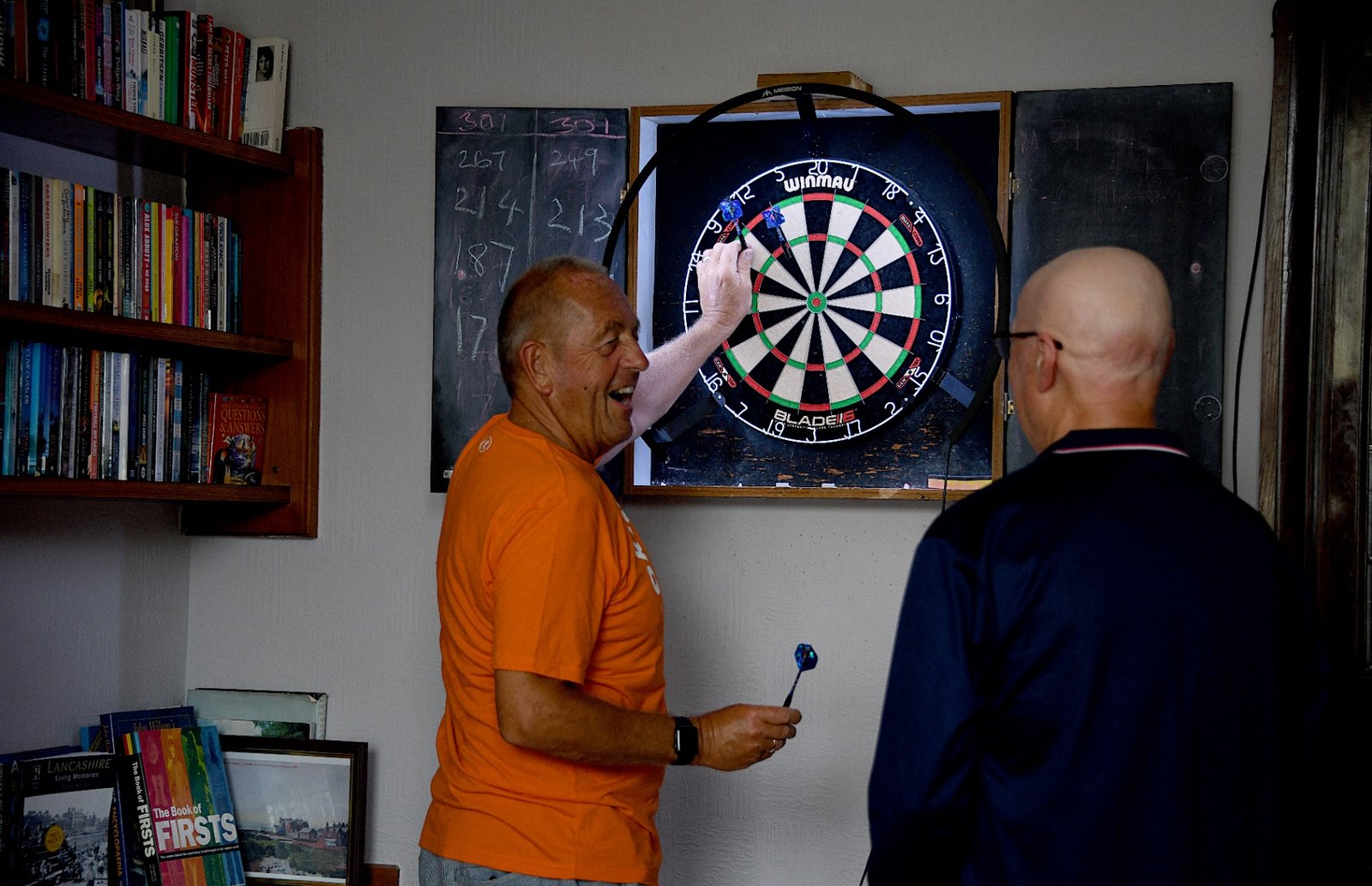 A member throwing at the club dartboard while another looks on