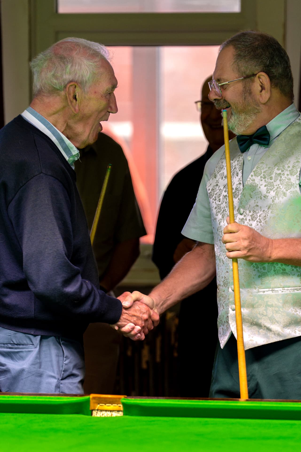Two players shaking hands across the snooker table at the end of a match.