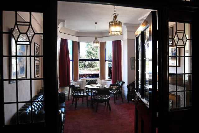 Looking into the Kilgrimol Room through its reinstated glass-panelled doors: bay window, deep red curtains, chesterfield and card tables.